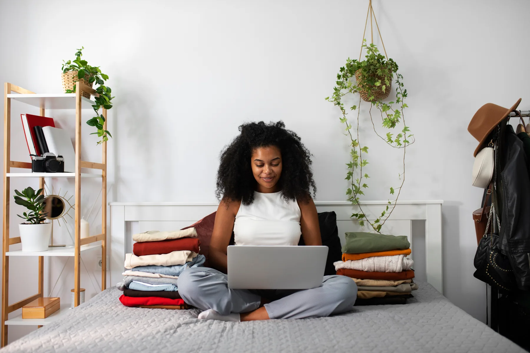 Woman on her bed with a laptop beside folded clothes